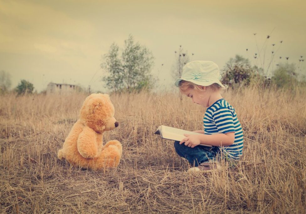 Cute girl reading book Teddy bear on the grass.